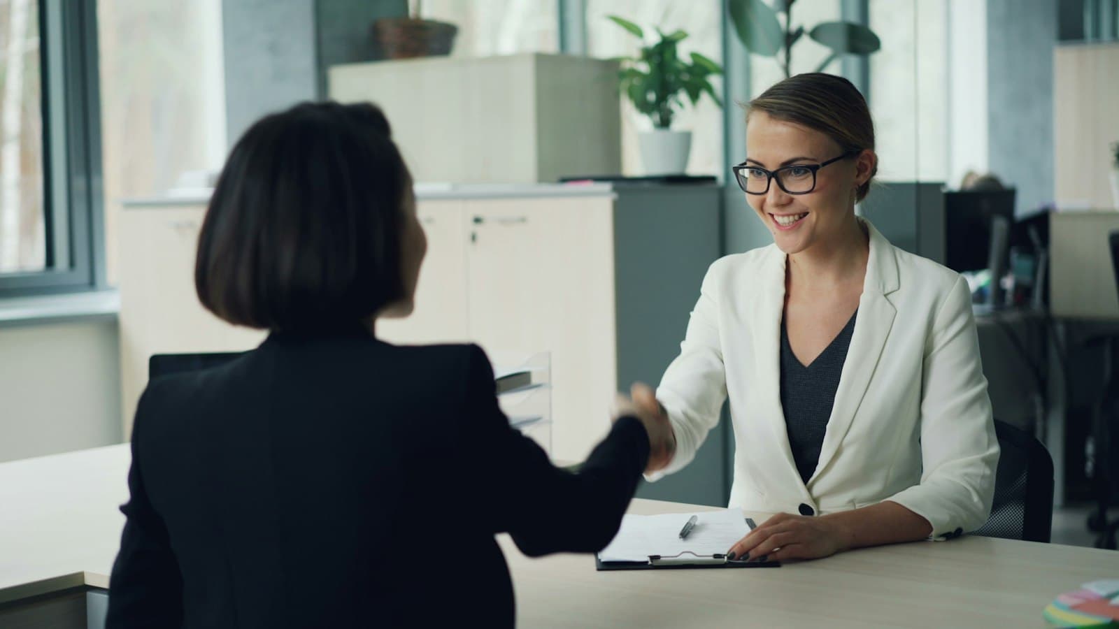 Twee vrouwen geven elkaar een hand over een bureau