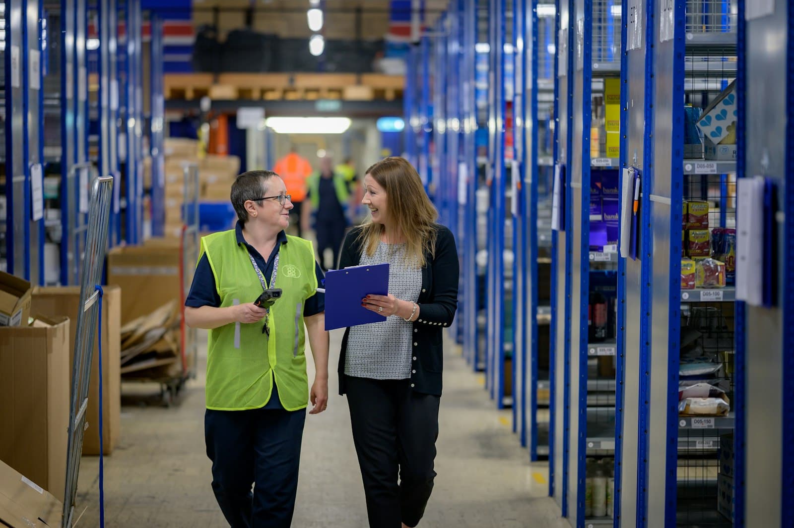 Twee vrouwen lopen met een klembord door een magazijn